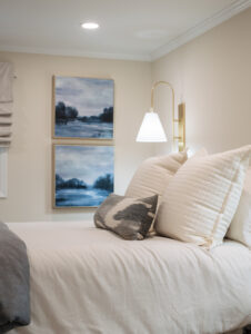 An image of a bed with white bedding and blue landscape wall art